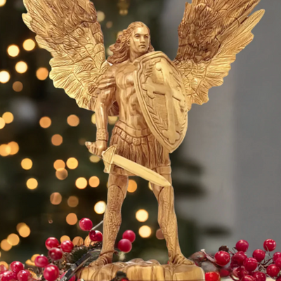 Wooden angel figurine with wings and a sword on a decorative base with berries, against a blurred light background.