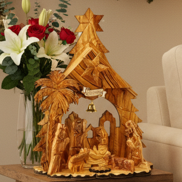 Wooden nativity scene with a star on top, placed next to a vase of flowers on a table.