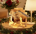 Wooden nativity scene with Mary, Joseph, and baby Jesus on a table with Christmas decorations.