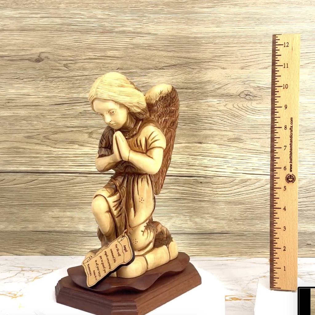 A wood carved angel statue in a praying position with an open book, set on a mahogany base, next to a ruler for scale.