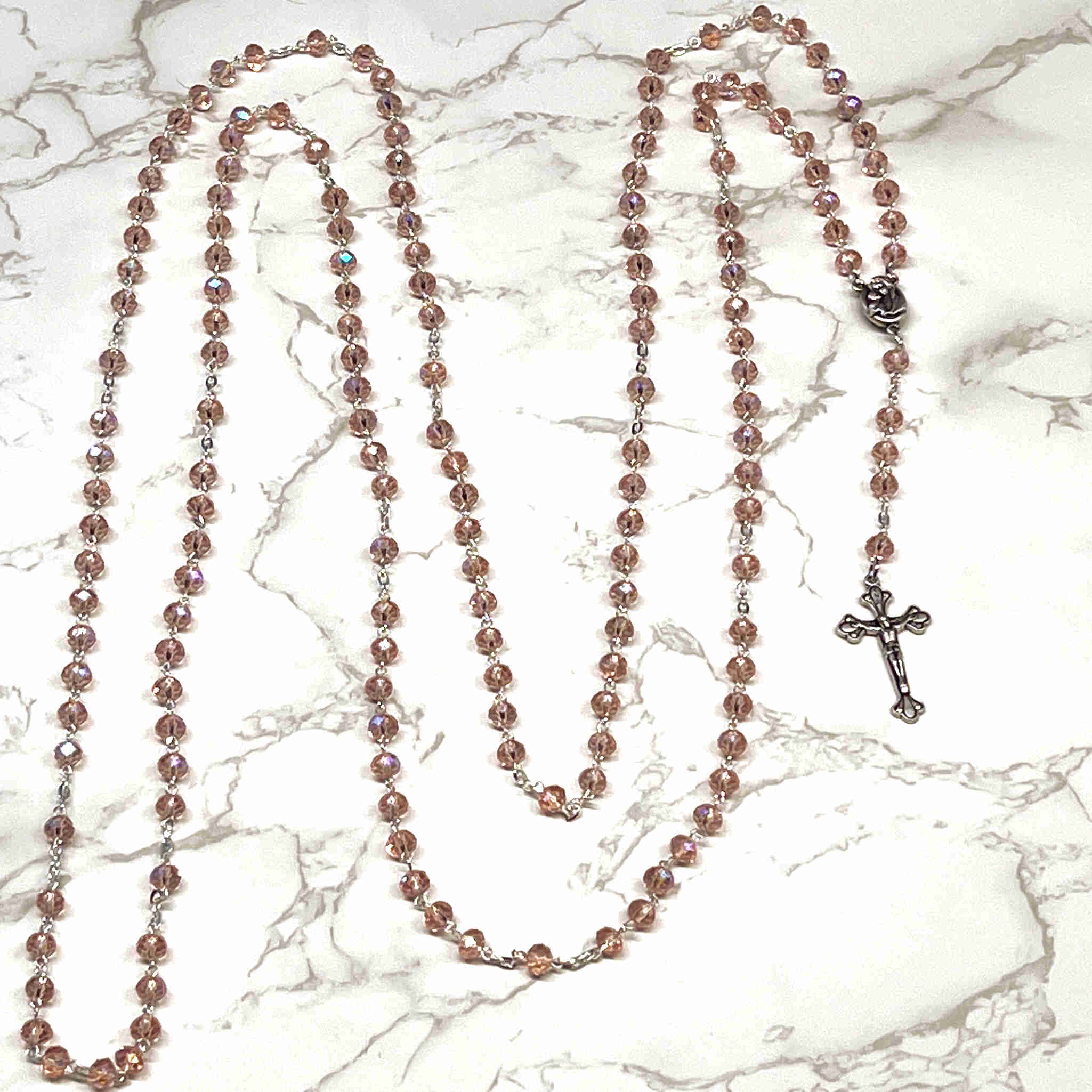 A 15 Decade Wall Rosary with pink crystal beads and a metal chain, placed on a marble surface.