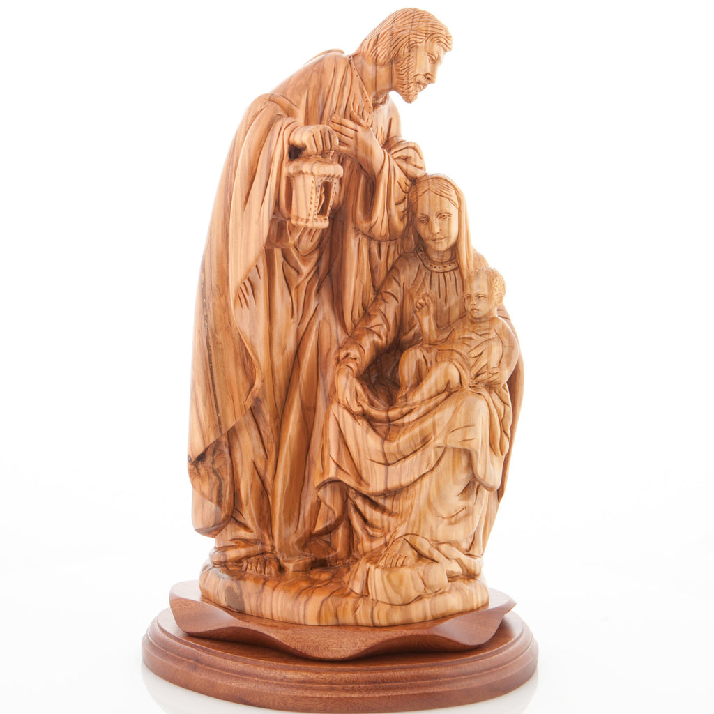An olive wood carved sculpture of the Holy Family holding a lamp, with Saint Joseph holding a lantern and Jesus being cradled by Mary.