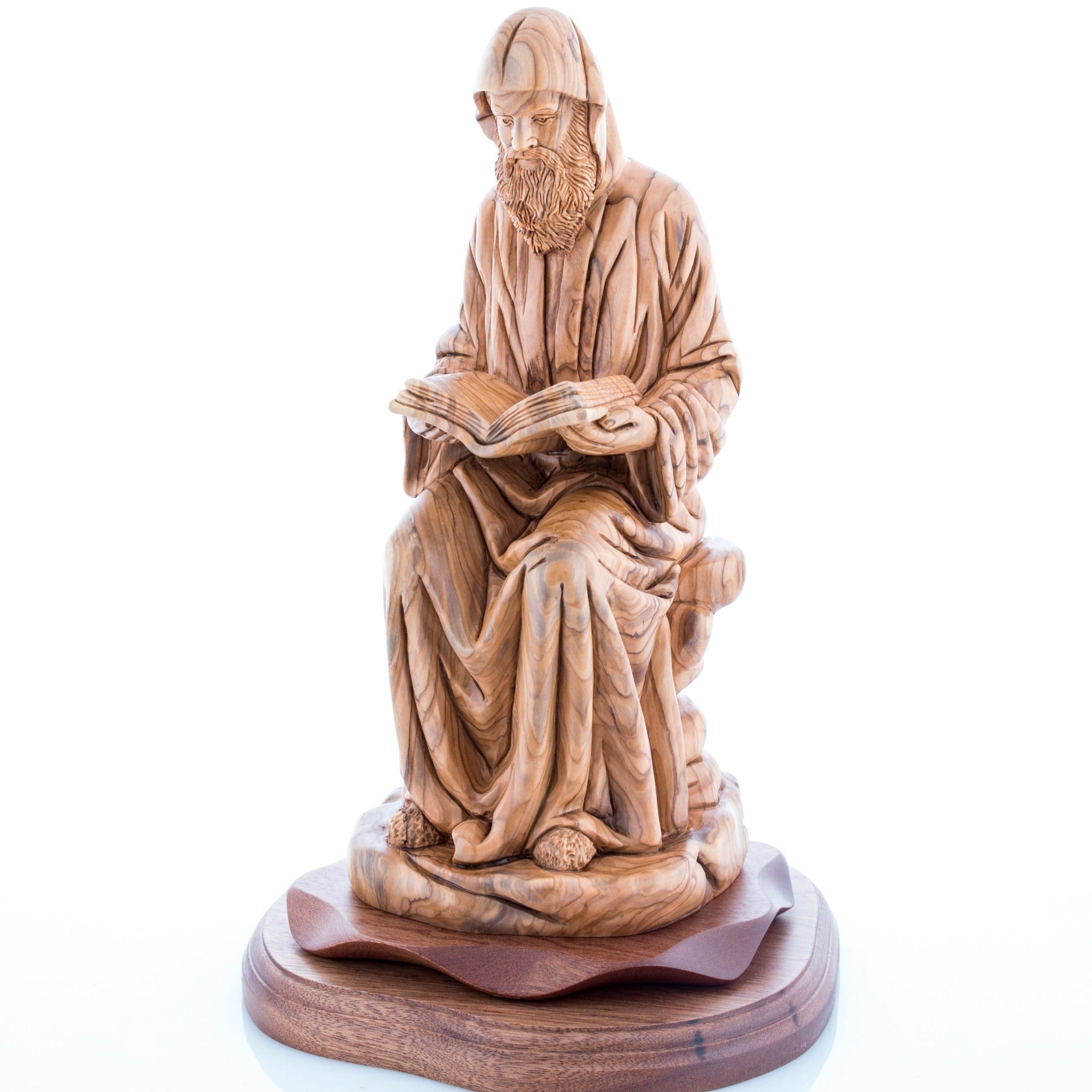 A carved wooden sculpture of St. Charbel, an elderly man with a beard and a book, sitting on a base.