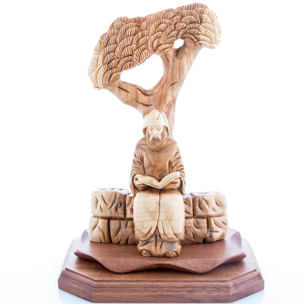 Wooden sculpture of St. Charbel sitting under a cedar tree, reading a book, carved from olive wood.