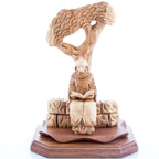 Wooden sculpture of St. Charbel sitting under a cedar tree, reading a book, carved from olive wood.