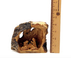 A small rustic nativity scene carved from olive wood, featuring figures of Jesus Christ, Virgin Mary, Joseph, and the star of Bethlehem, with a measuring tape for scale.