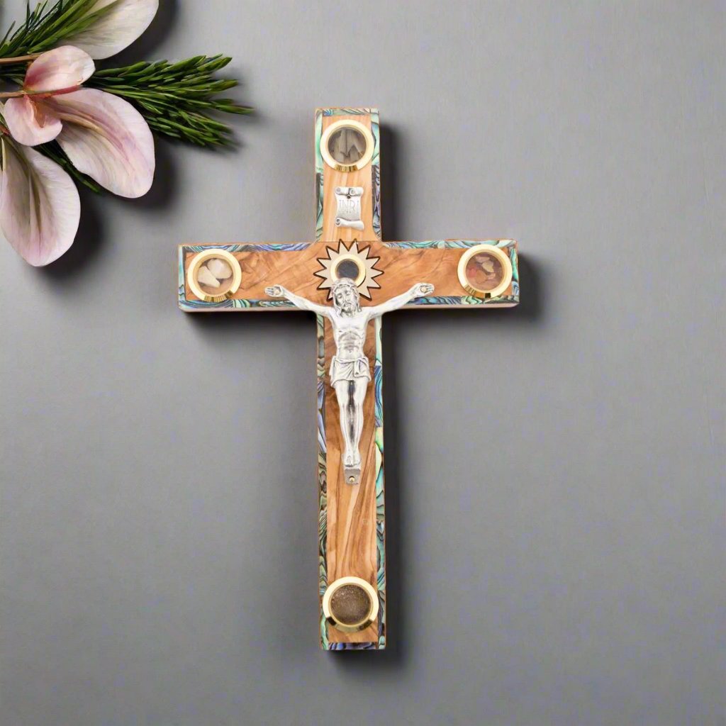 A wall-mounted crucifix made of olive wood with mother of pearl inlays, featuring five glass capsules with souvenirs from the Holy Land, displayed against a neutral background.
