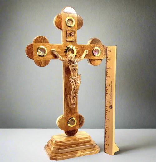 A wooden standing crucifix with a 2.5-inch base, featuring carved details and five glass capsules with souvenirs from the Holy Land placed on and around the cross.
