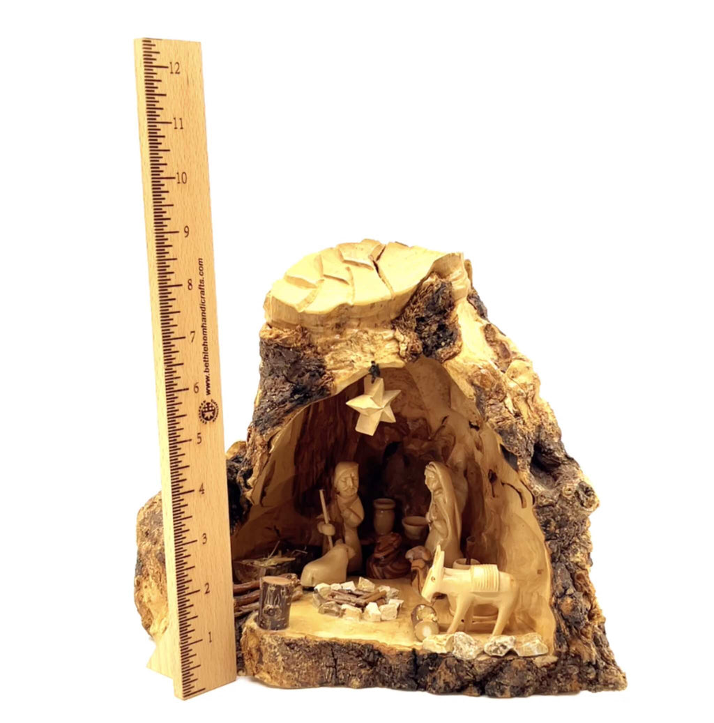 Rustic nativity scene made of olive wood, featuring figures of Jesus, Mary, and Joseph in a stable-like setting, with a natural bark finish and a ruler for scale.